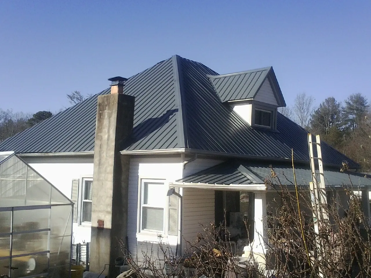 Dark blue standing seam metal roof on a white farmhouse with dormer — Slate & Tile Roof Repair by Roofing Brothers in Goochland
