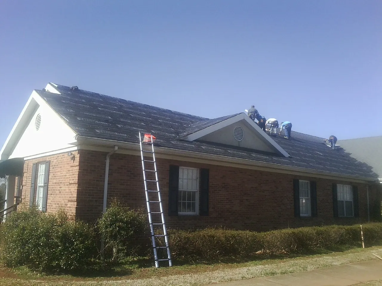 Crew tearing shingles off a brick ranch roof with a ladder set — Emergency Roof Repair work by our crew in Goochland