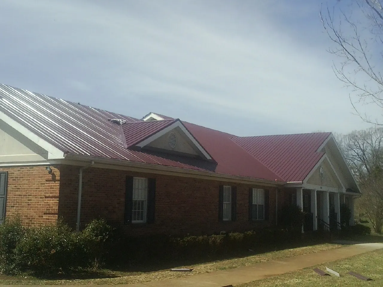 Red metal roof with gabled entries on a long brick building, from a Hail Damage Roof Repair job in Goochland