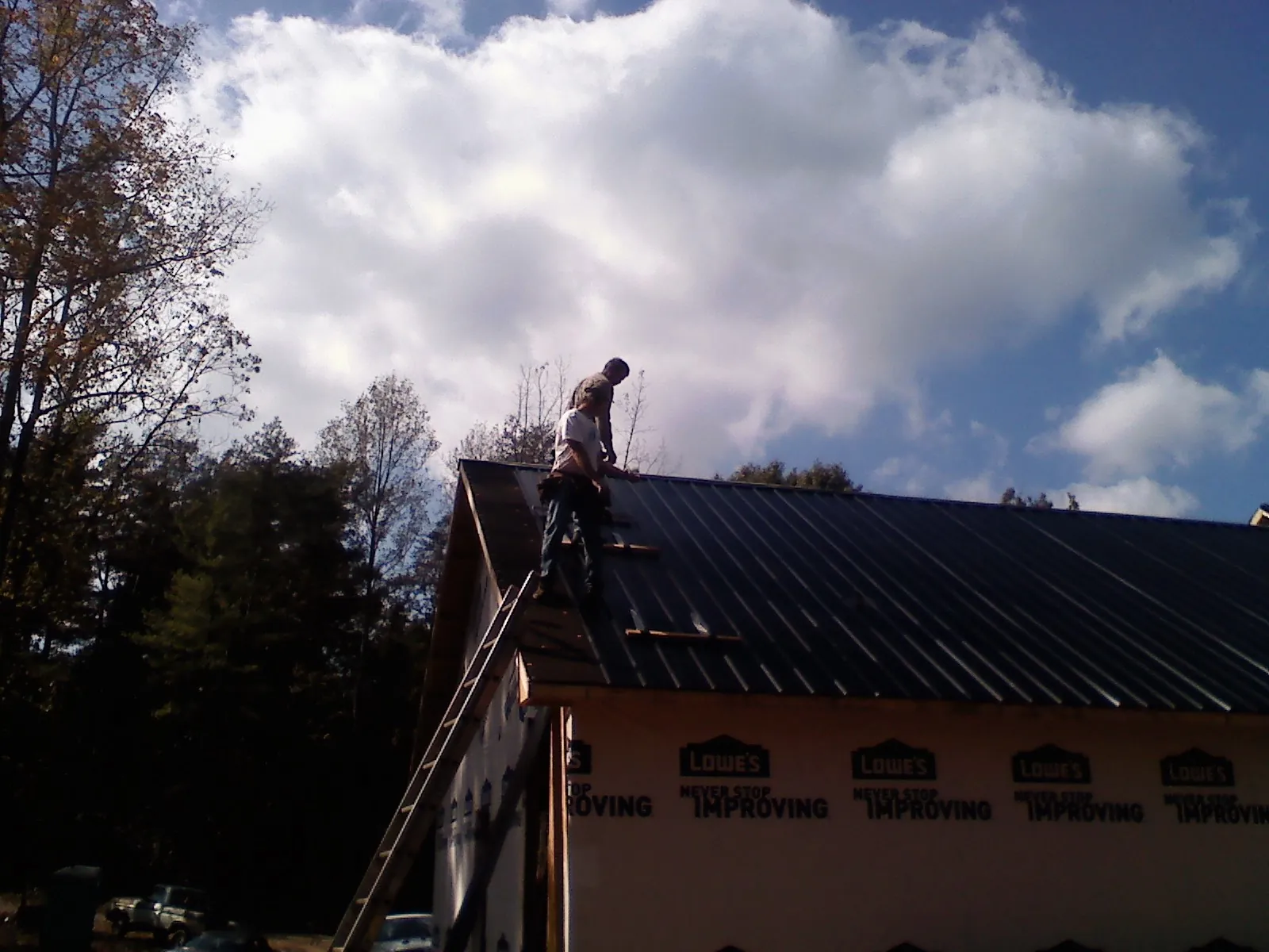 Roofer fastening dark metal panels high against a cloudy sky, from a Roof Inspection job in Goochland