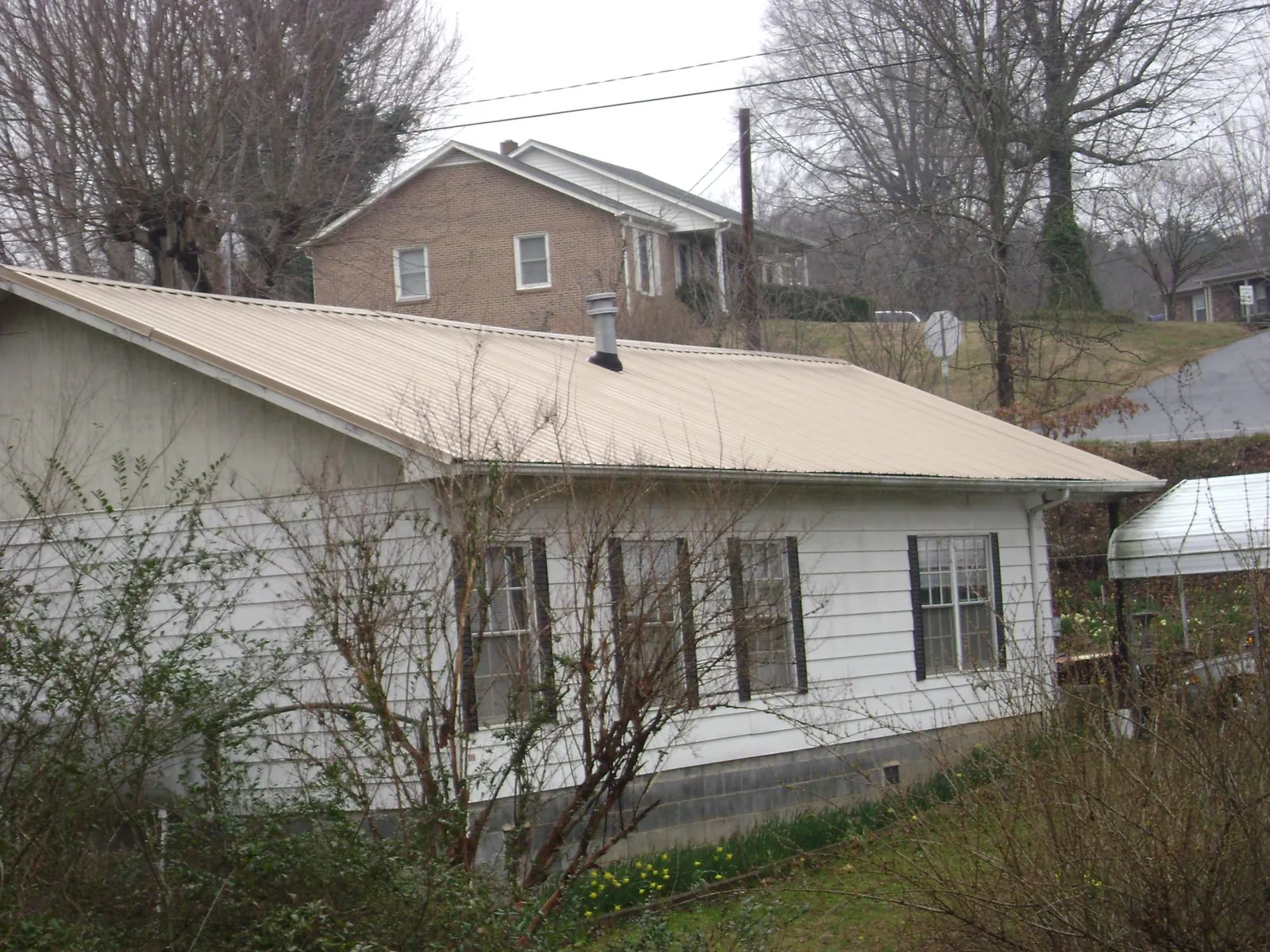 Tan metal roof on a white sided house set into a hillside — Commercial Roofing by Roofing Brothers in Goochland