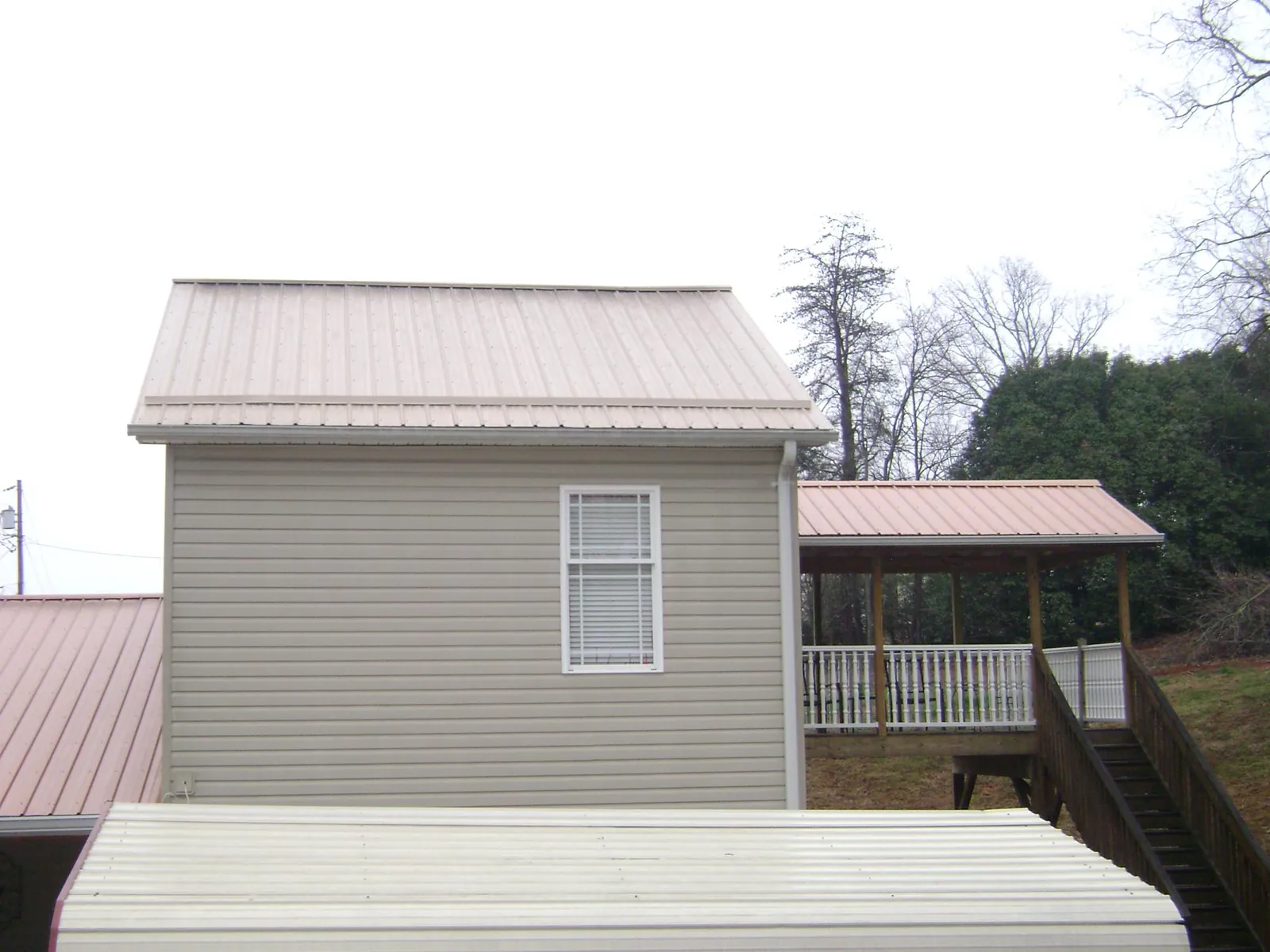 Tan metal roofs on a two story addition and attached porch, from a Roof Replacement job in Goochland